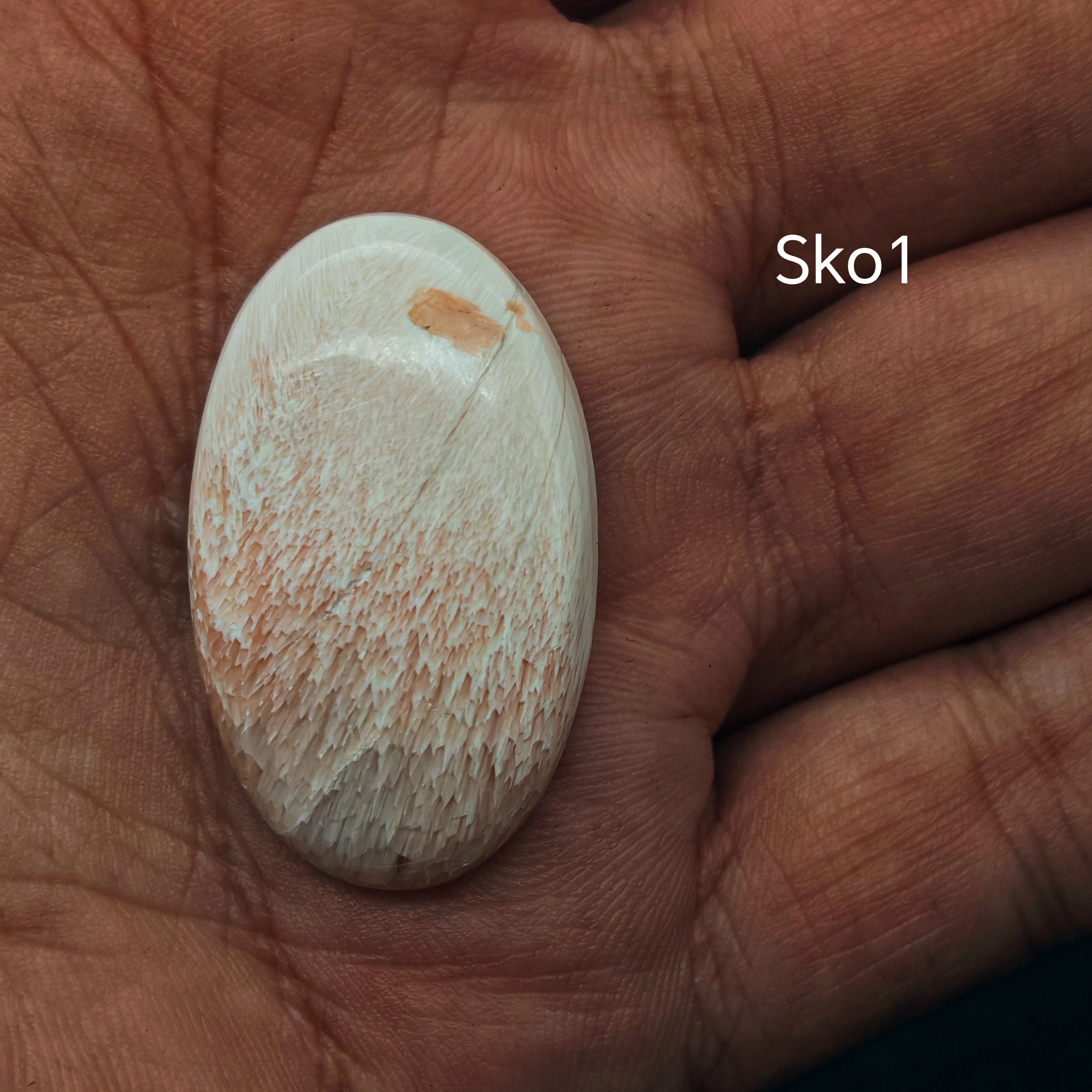 Kézben forgatott fehér szkolecit kaboson, gyöngyházfényű felülettel