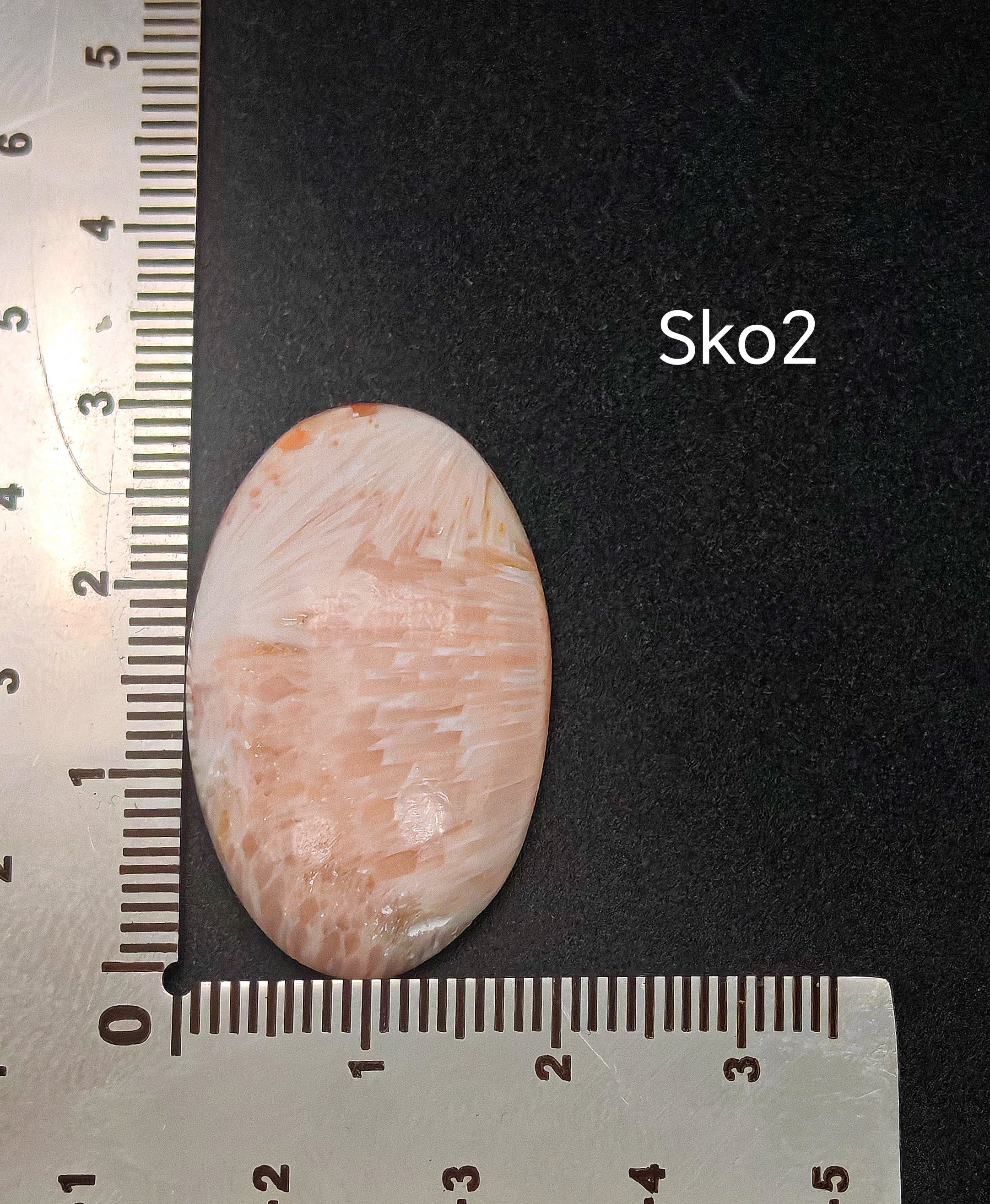 Fehér szkolecit kaboson vonalzón mérve, kb. 4,76 g súlyú természetes drágakő