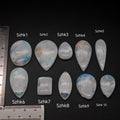 Természetes szivárványos holdkő (rainbow moonstone) kaboson kövek sorban számozva, fehér alapon, méretjelzéssel — a kép sorrendje megegyezik a videóban látható kövek sorrendjével