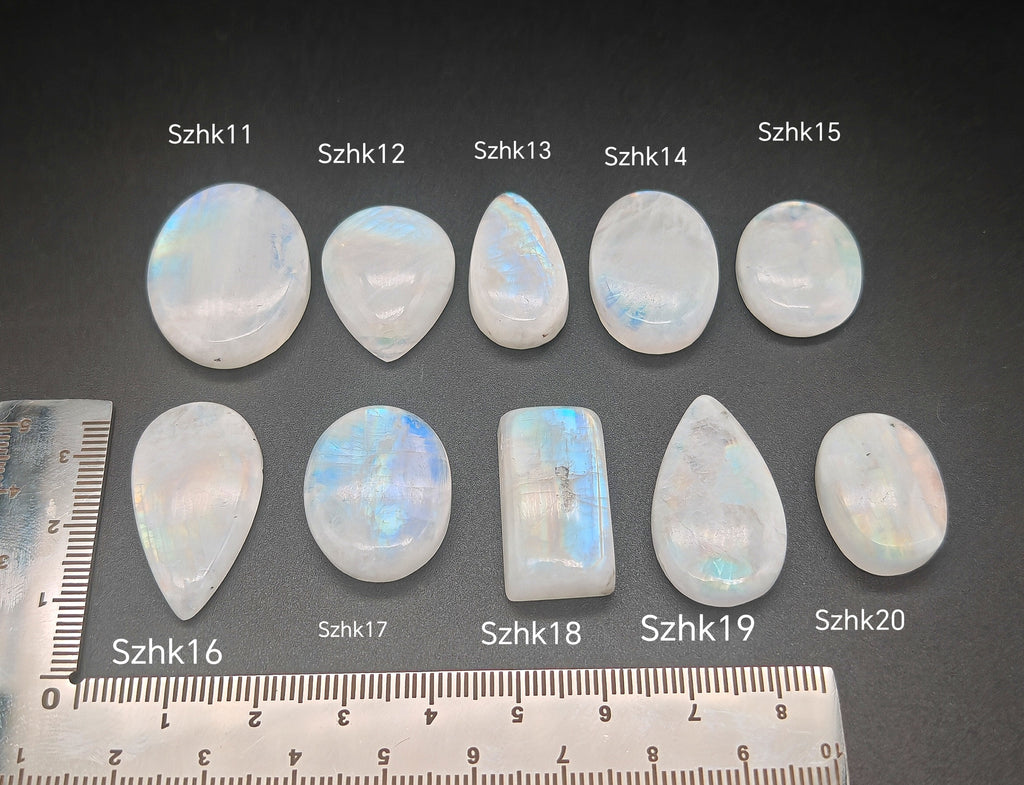 Természetes szivárványos holdkő (rainbow moonstone) kaboson kövek sorban számozva, fekete alapon, méretjelzéssel — a kép sorrendje megegyezik a videóban látható kövek sorrendjével