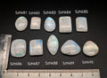 Természetes szivárványos holdkő (rainbow moonstone) kaboson kövek sorban számozva (Szhk81–Szhk90), fehér alapon vonalzóval, különböző alakokban — a kép sorrendje megegyezik a videóban látható kövek sorrendjével