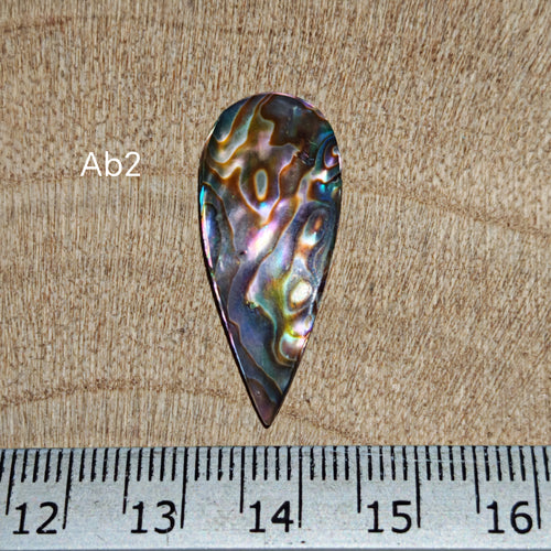Abalone kagylóhéj kaboson, Ab2, csepp alakú, kék, lila, ezüst és türkiz irizáló színekkel, milliméteres vonalzó mellett.