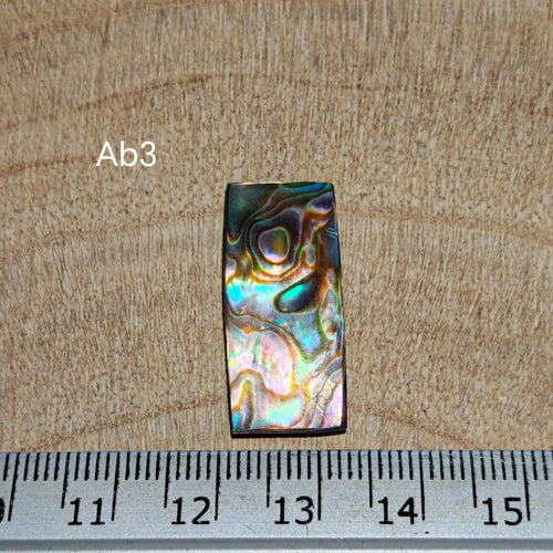 Abalone kagylóhéj kaboson, Ab3, téglalap alakú, türkiz, kék, arany és halvány rózsaszín irizáló színekkel, milliméteres vonalzó mellett.