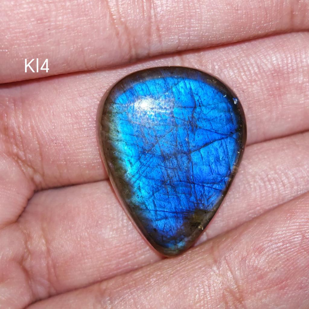 Kék labradorit kaboson, Kl4, lekerekített csepp formájú, élénk elektromos kék és türkiz fénnyel, finom ezüstöskék vonalakkal és sötét szegéllyel, tenyéren tartva.