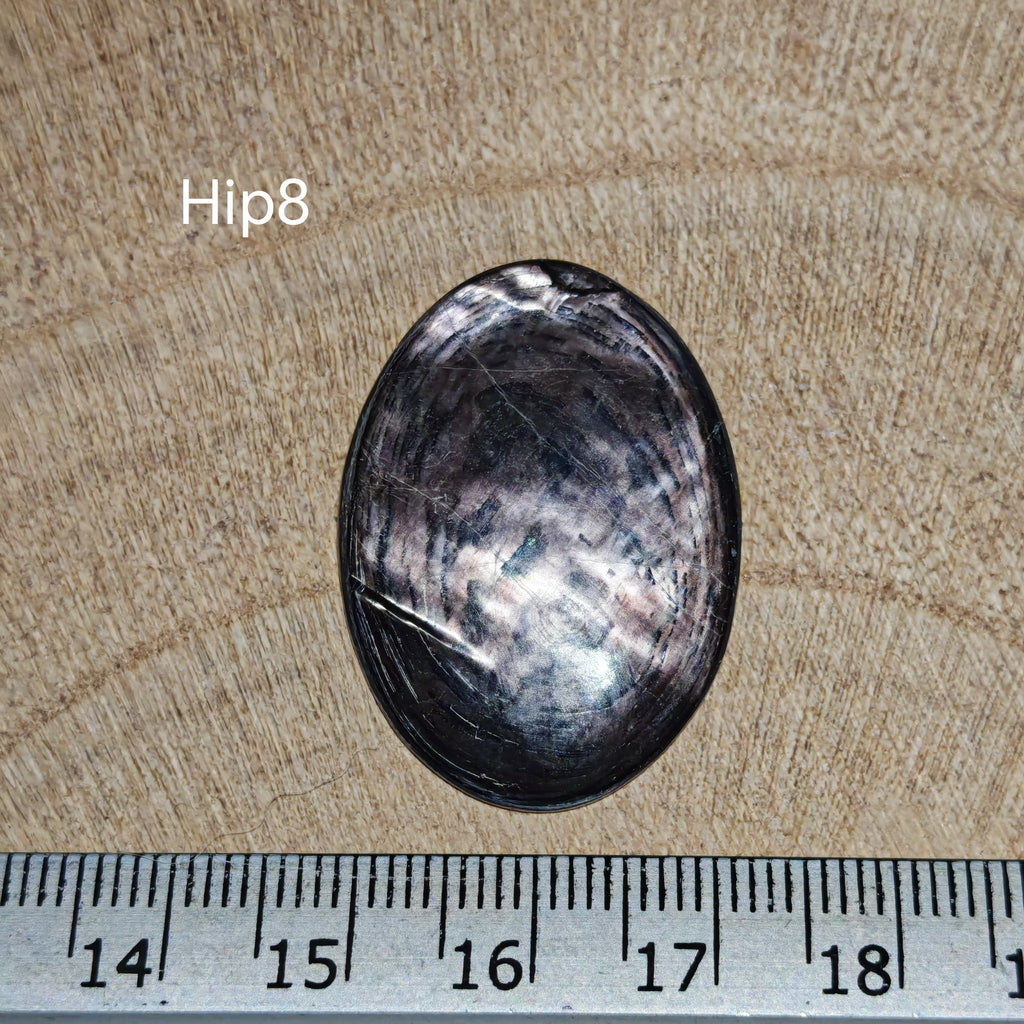 Hypersthene kaboson, Hip8, ovális formájú, ezüstösen csillogó felülettel és sötét szegéllyel, milliméteres vonalzó mellett.