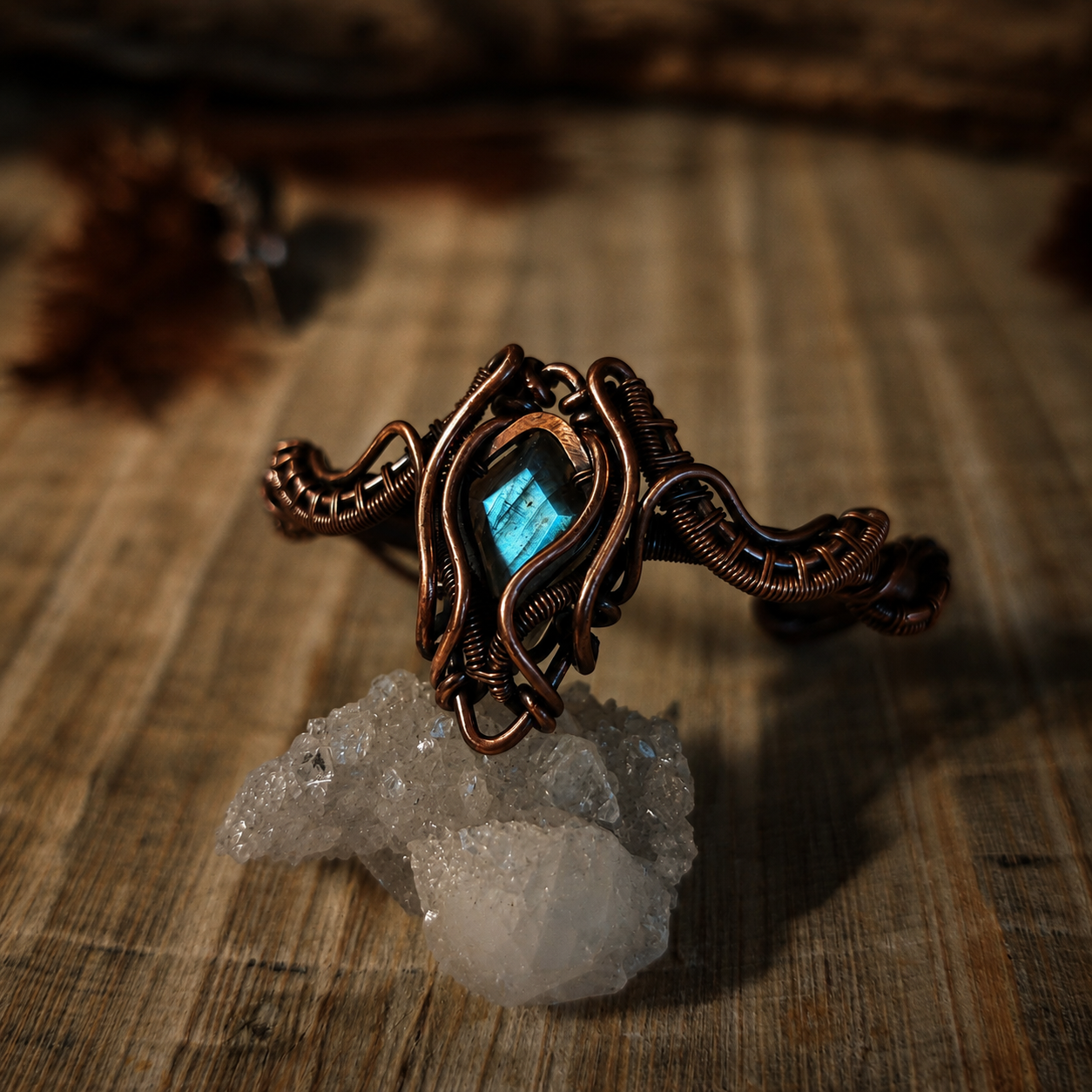 Eye of Balor labradorit kézzel készített vörösréz drótfonásos karperec kvarc kristályon, rusztikus fa háttérrel – YourCrystal